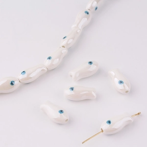 Detailed view of fish-shaped ceramic beads with blue evil eye motifs for DIY jewelry