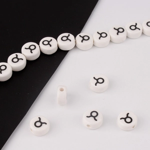 Close-up of white ceramic Taurus zodiac beads showing the black symbol and threading holes