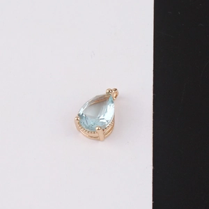 Macro detail of a pear-shaped light blue crystal pendant with a gold plated beaded setting