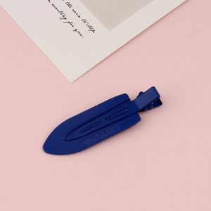 Close-up of a matte dark blue seamless hair clip with embossed logo on pink background