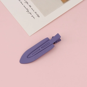 Close-up of matte purple metal hair clip with embossed detail on soft pink background