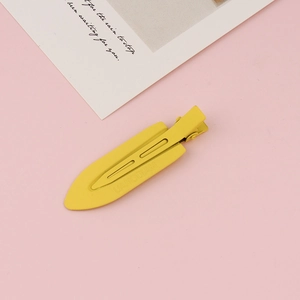 Detailed view of a yellow matte finish duckbill hair clip on a pink aesthetic background