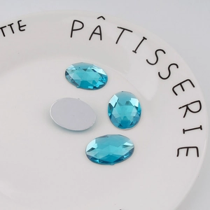 Detail view of 18x25mm oval flatback lake blue acrylic rhinestones on a white plate