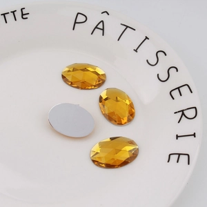 Macro detail of amber yellow oval flatback acrylic rhinestones on a decorative white plate