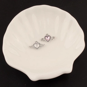 Macro detail of Y2K silver wing heart pendants with pink gemstone in white tray
