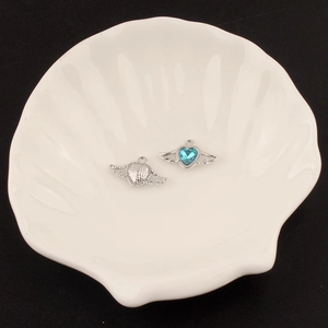 Detailed close-up of a Y2K winged heart alloy pendant with blue crystal on a shell tray