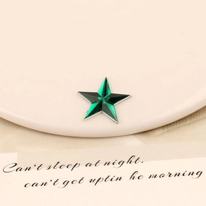 Macro shot of green faceted star acrylic rhinestone with silver edge in a ceramic tray