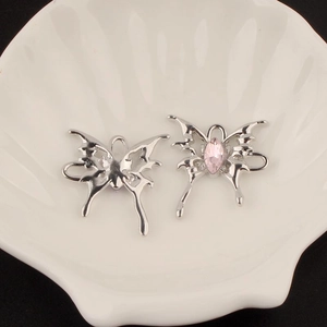 Detail of silver alloy butterfly pendant and ear cuff with pink crystal on shell tray