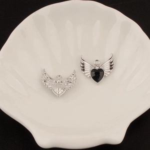 Detailed macro view of Y2K silver heart wing charms with black inlay on a shell tray