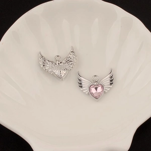 Detailed view of silver angel wing heart charms with pink zircon in a shell tray