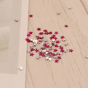 Détail de paillettes à ongles étoiles 3mm roses et argentées sur surface en bois