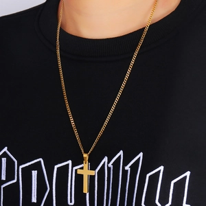 Close-up of a polished gold cross pendant necklace worn by a model on a black background