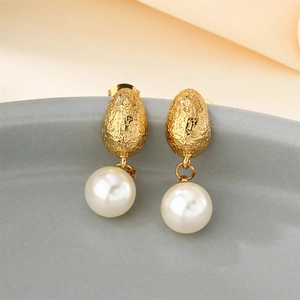 Eleganti orecchini ovali dorati testurizzati con perle bianche su un piatto di ceramica
