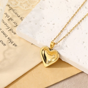 Collier avec pendentif cœur doré poli miroir sur un bloc texturé blanc minimaliste