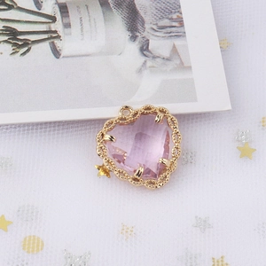 Macro shot of pink heart-shaped crystal pendant with gold lace metal frame and loop
