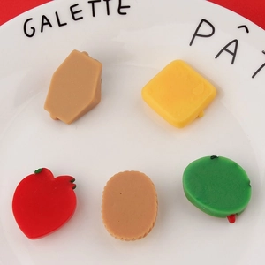 Mini DIY resin charms in fruit and pastry shapes on white ceramic plate with red background