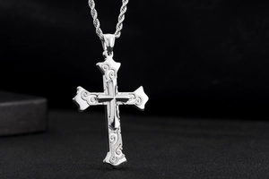 Detail of silver layered cross pendant with scroll engravings and textured matte finish