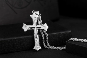 Detailed macro view of vintage cross pendant with intricate scroll patterns and rope chain