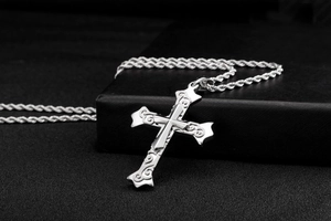 Macro detail of silver layered cross pendant with vintage scrollwork on a rope chain