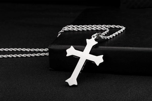 Close-up of brushed silver cross pendant with unique wavy edges on a metal rope chain