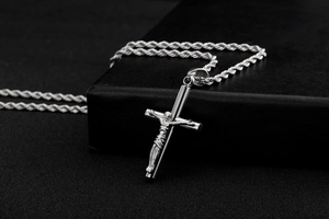 Détail du pendentif croix en acier inoxydable avec relief de Jésus sur support en cuir