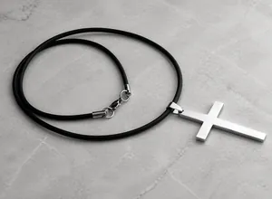 Macro detail of silver stainless steel cross pendant with brushed texture and black leather cord