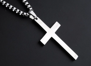 Macro shot of polished silver stainless steel cross pendant on black leather surface
