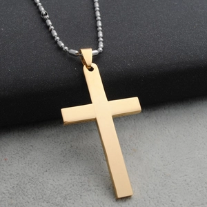 Detailopname van een gladde gouden kruishanger met een zilveren bolletjesketting op zwarte stof
