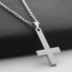 Macro shot of silver inverted cross pendant in polished stainless steel on a dark stand