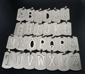 Flat lay of 26 stainless steel capital A-Z alphabet dog tags with brushed metal texture