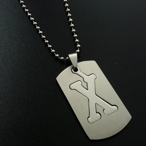 Macro detail of brushed stainless steel necklace showing cutout letter X pendant with ball chain