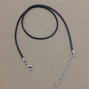 Detalle de collar de cordón negro con cierre de langosta plateado y cadena de extensión en marrón