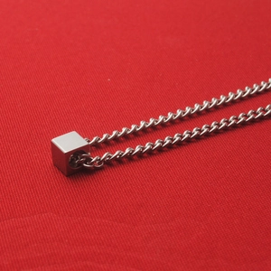 Minimalistische Edelstahlkette mit kleinem Würfelanhänger auf rotem Hintergrund