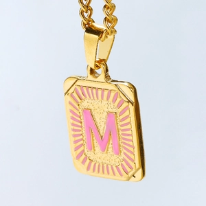 Detail van 18k vergulde rechthoekige hanger met roze emaille letter M en zonnestraal-design