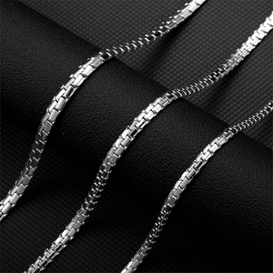 Detailed close-up of a high-polished silver box chain necklace on a black textured surface