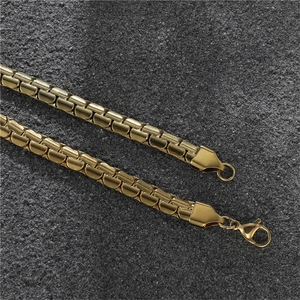 Detailed close-up of golden stainless steel curb chains with lobster clasp on dark background