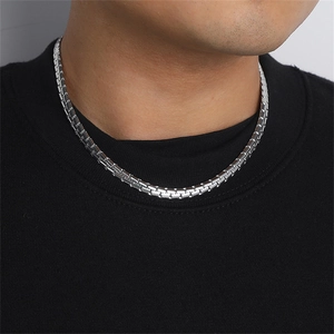Close-up of a silver polished stainless steel box chain necklace worn by a model