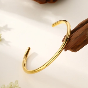 Bracelet jonc en C en acier inoxydable doré 18 carats sur un présentoir en bois rustique