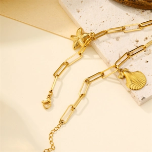 Gold paperclip chain anklet with starfish and shell charms on stone background