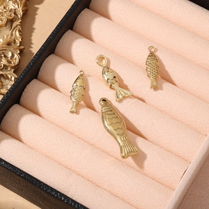 Macro detail of 18K gold plated fish charms with scale texture on pink velvet