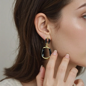 Dettaglio degli orecchini pendenti geometrici nero e oro indossati da una modella