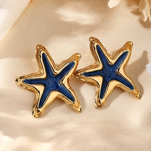 Detalle de pendientes de estrella de mar dorados con esmalte azul sobre satén