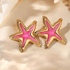 Vista macro detallada de pendientes de estrella de mar en esmalte rosa sobre seda champán