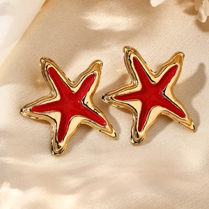 Detalle de los pendientes de estrella de mar dorada con esmalte rojo sobre raso champán