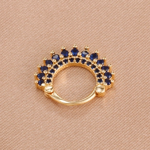 Golden crown septum ring with dark blue crystals on champagne silk background