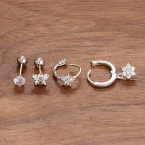 Detailed set of four silver stainless steel flower and zircon stud earrings on wood