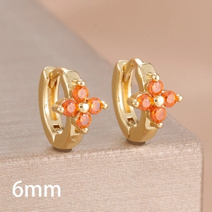 Macro shot of 6mm gold huggie earrings featuring vibrant orange clover-shaped zirconia