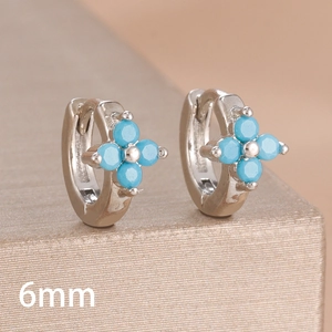 Close-up of 6mm silver four-leaf clover earrings with blue zircon stones on a gold stand