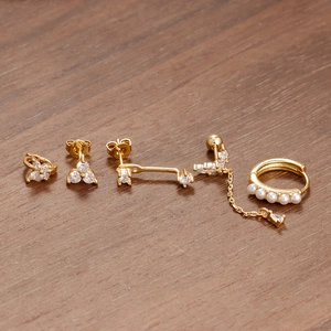 Detail von fünf goldenen Sternohrringen mit weißen Zirkonia und Perlen auf Holz