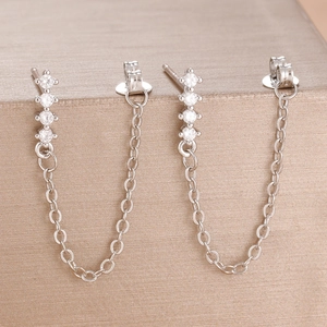 Macro shot of silver zircon chain earrings hanging on a champagne jewelry box edge
